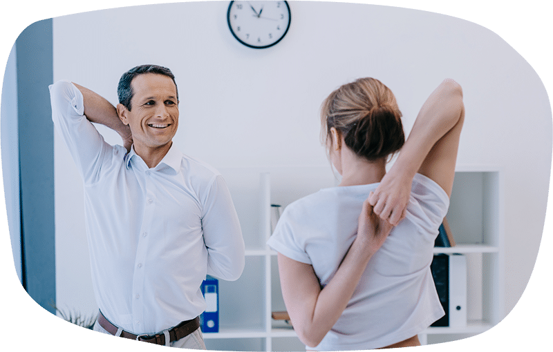 Ein Mann und eine Frau stehen sich lächelnd gegenüber und führen eine Dehnübung für die Schulter durch. Das Bild steht repräsentativ für gesundheitsfördernde Maßnahmen zur Stärkung der emotionalen Bindung zwischen Unternehmen und ihren Mitarbeitenden.