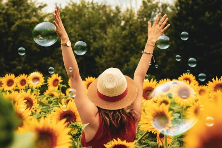 Eine Frau von hinten, wie sie in einem Sonnenblumenfeld steht und die Hände in die Luft streckt. Wie funktioniert das Belohnungssystem des Gehirns? (What is the brain reward system?)