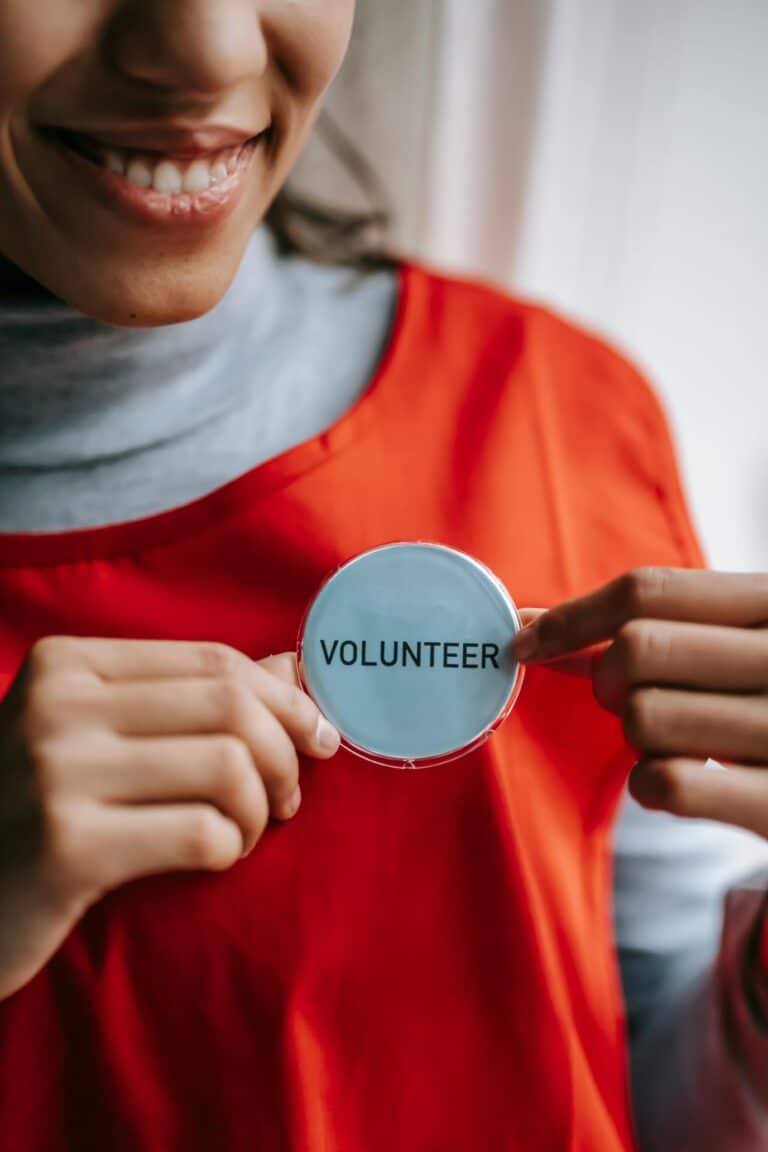 Eine Frau lächelt und hält ihr Volunteer Schild in die Kamera.